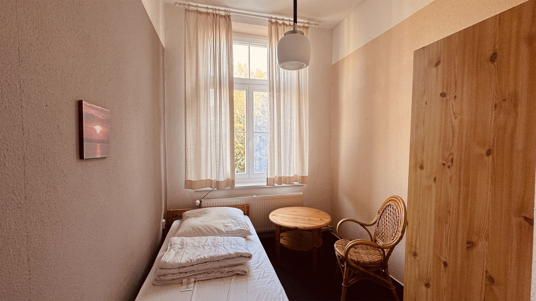 Einzelzimmer mit Bett, Tisch und Kleiderschrank